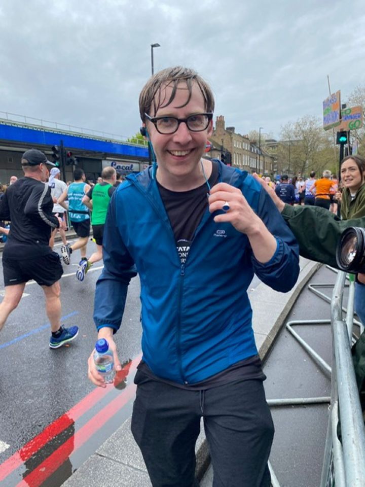 Ross, smiling, holding a small bottle of water in one hand after a run